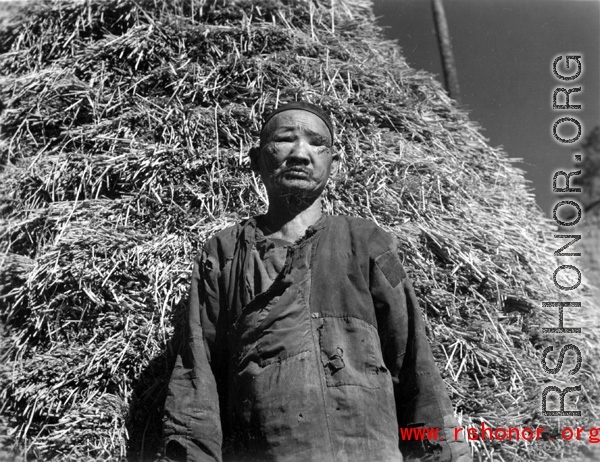A blind villager in China poses for photographer with a stack of rice straw behind. During WWII.