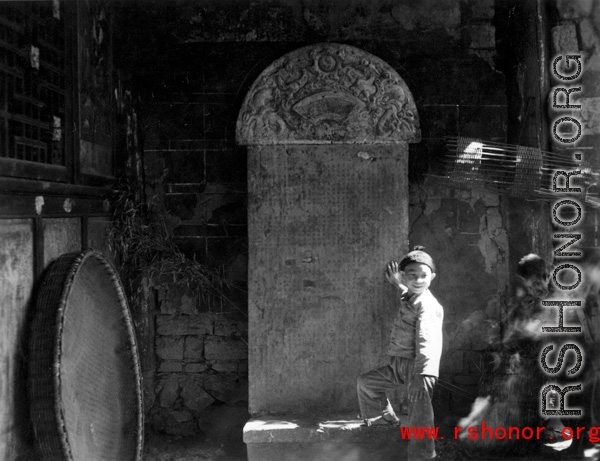 During WWII a boy stands in front of a stone tablet in the entry area of a temple or other building, probably in Yunnan province.