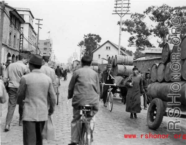 A street scene in either Songming  or Kunming, in Yunnan province, China, during WWII. Notice the 55-gallon barrels being hauled away for reuse after flying over The Hump.  From the collection of Eugene T. Wozniak.