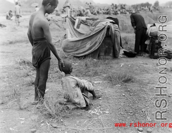 A gravely ill boy is supported by an adult: The sick and weakened during the Chinese civilian evacuation in Liuzhou city Guangxi province, China, during WWII, during the summer or fall of 1944 as the Japanese swept through as part of the large Ichigo push.
