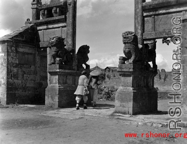 Two women walk through a ceremonial gate in Yunnan province during WWII.
