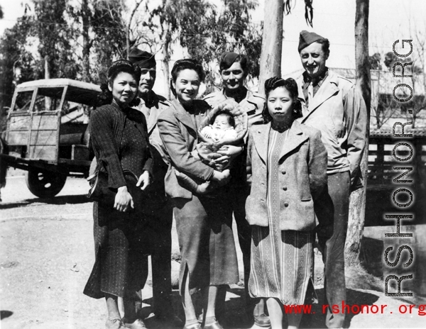 An elite Chinese woman holds a baby, and poses with American servicemen and local people in Yunnan province, China, during WWII.