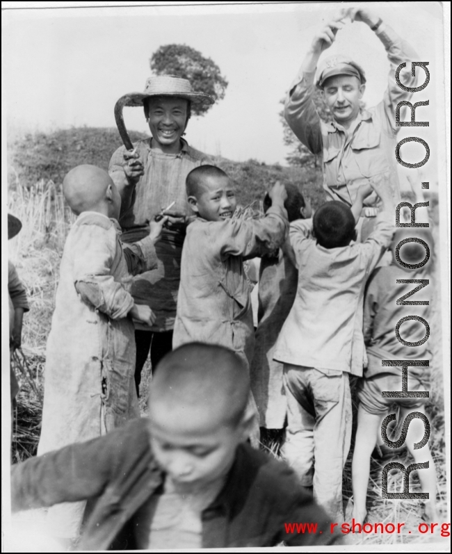 A GI hands out treats (likely candy) to enthusiastic Chinese kids as a farming woman smiles. During WWII.