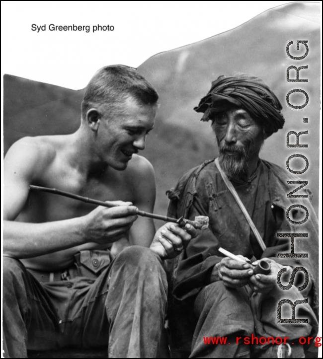 A GI inspects smoking pipe of local man in China, while local man holds western-style pipe. During WWII.  Photo by Syd Greenberg.