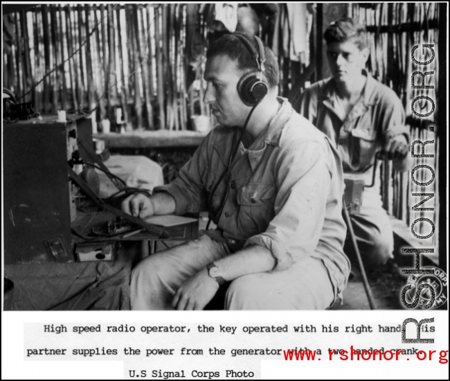 High speed radio operator working from a bamboo hut in the jungle, the key operated by his right hand. His partner supplies the power from a generator with a two-handed crank.  US Signal Corps photo.