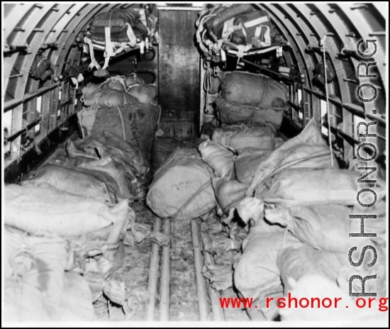 Bags are piled in cargo plane ready for aerial drop to Allied troops. Some will be dropped with parachutes to slow the drop (those in the distance in the image), and some will be dropped directly. In the CBI.