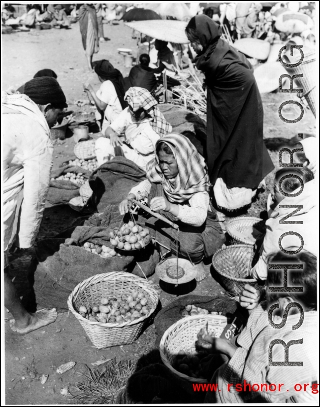 Women weight out produce for sale at a farmer's market in the CBI during WWII.