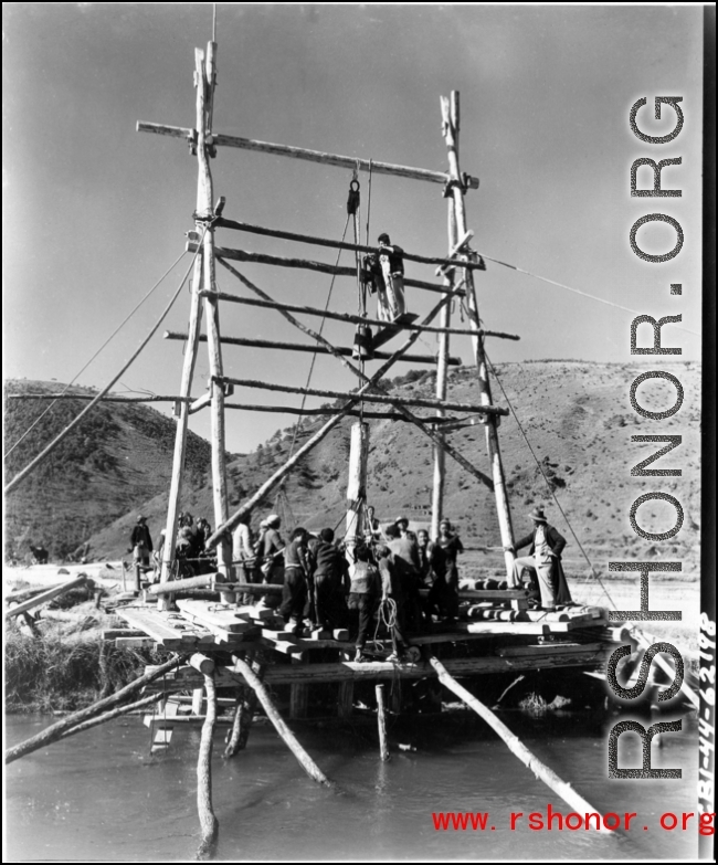 A pole driver, built on-site, is employed by workers in SW China to drive bridge supports into the ground. During WWII.