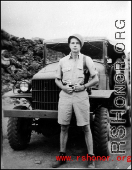 A GI stands in front on a truck on a road in the CBI during WWII.