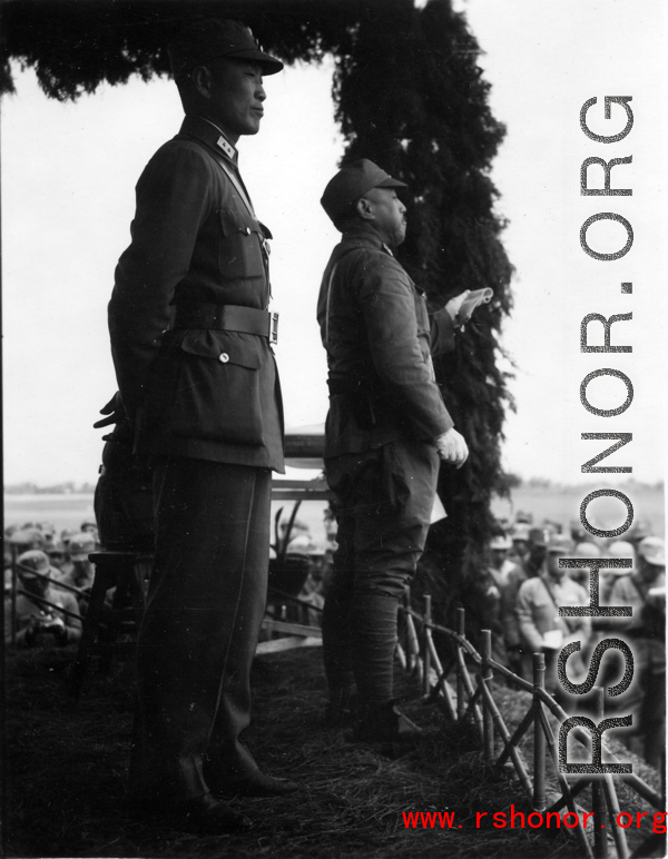 Chinese Lt. General Du Yuming, commander of Nationalist 5th Corps (第五集团军总司令兼昆明防守司令杜聿明) looks out at troops, with Gen. Wei Lihuang (卫立煌) facing assembled troops, and another person holding a sheet of paper, on stage during rally.