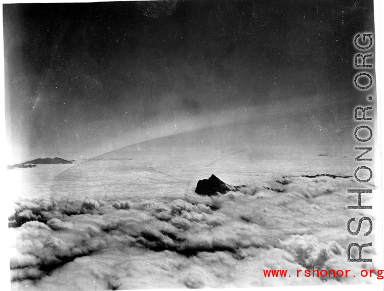 A mountain pokes through the clouds during a war time flight of US planes.