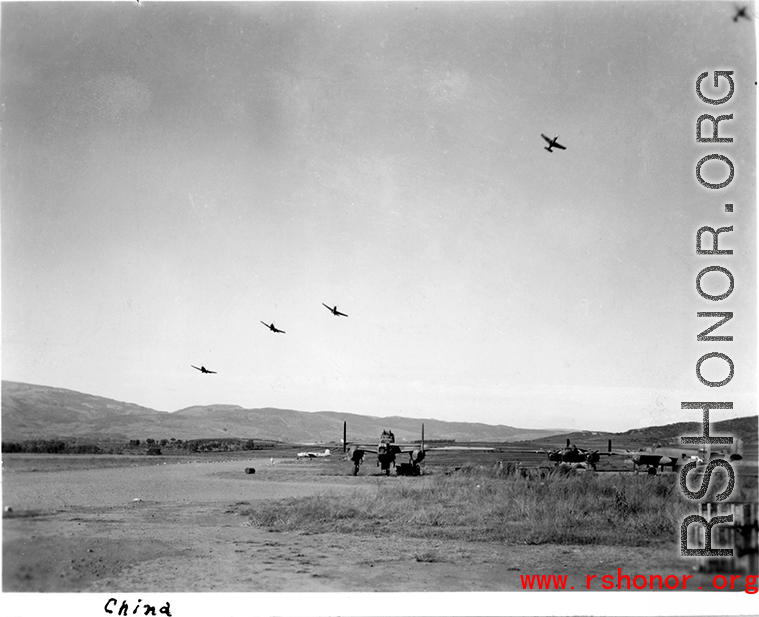 Several P-40 fighters pass over the runway and begin a "break out" to land at Yangkai, Yunnan province. American B-25H bomber are visible in the foreground of this picture taken in the CBI.