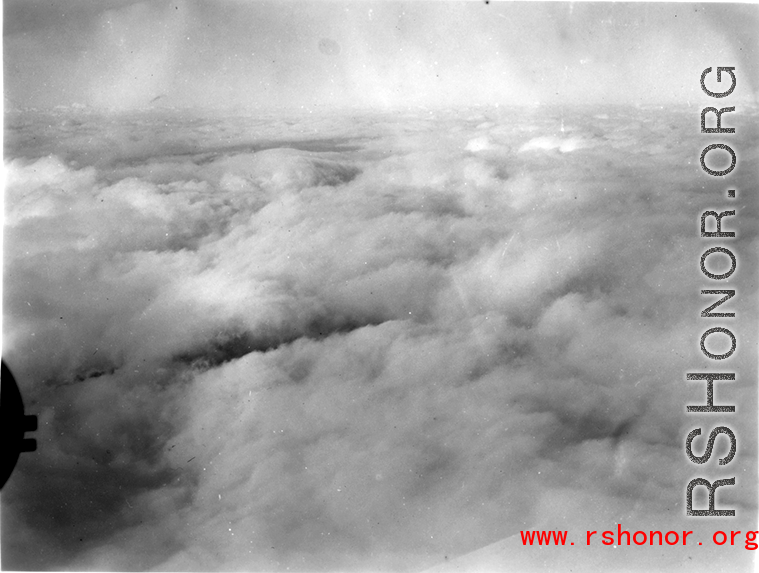 A cloudy landscape below as seen the air from an American bomber (likely a B-25) during WWII.