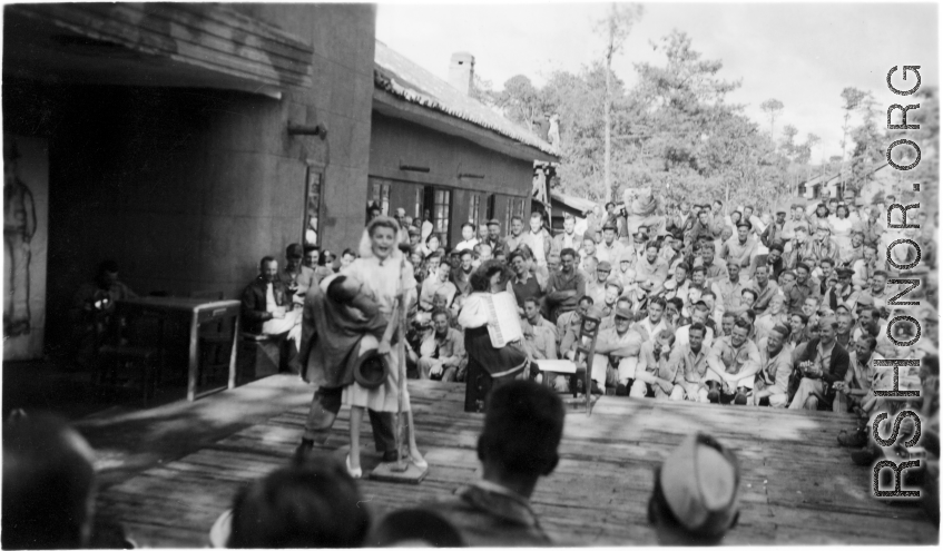 Celebrities (including Ann Sheridan hamming it up with Ben Blue, and Ruth Dennis playing an instrument in this shot) perform on an outdoor stage set up at the "Last Resort" at Yangkai, Yunnan province, during WWII. Notice both Americans and Chinese in the audience for this USO event.