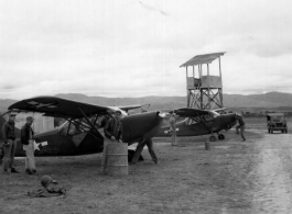 A pair of Stinson L-5's at a base in China, possibly Yangkai.  Notice the man in the background starting the plane, and the simplified control tower.