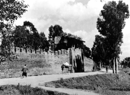 A section of city wall and gate to Chenggong (Chengkung), possibly going back to the final days of the Ming Dynasty, 400 years before. Two Chinese men carry a wealthy Chinese merchant on a “hua-gan" (滑竿) pole chair.