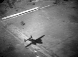 Aerial view of structures and shadow of B-25 in Burma or French Indochina, in the CBI, during WWII.