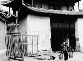 People come and go from village gate in SW China during WWII, with propaganda and military rules posed beside the gate.