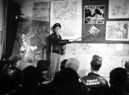 A pre-flight briefing for American flyers in China during WWII.. The maps on the wall behind the speaker clearly show Hong Kong harbor, which the Japanese controlled.