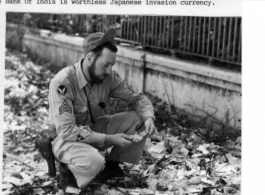 Frank Bond examines discarded "invasion currency" on a Rangoon, Burma, street near Bank of India, where it had been dumped during evacuation. Spring 1945.