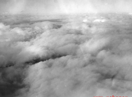A cloudy landscape below as seen the air from an American bomber (likely a B-25) during WWII.