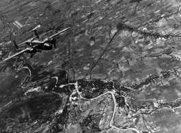 B-25 Mitchells fly away from a recently bombed town, with a confluence of road and railway bridges right in the smoking bombed area.  Probably in SW China, Indochina, or the China-Burma border region. During WWII.