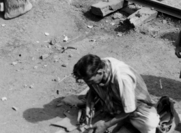 Man does shoe repair with simple tools next to the railway. In India.  Scenes in India witnessed by American GIs during WWII. For many Americans of that era, with their limited experience traveling, the everyday sights and sounds overseas were new, intriguing, and photo worthy.