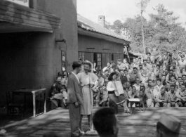 Celebrities (including Ann Sheridan, Ben Blue, and Ruth Dennis on instrument in this shot) perform on an outdoor stage set up at the "Last Resort" at Yangkai, Yunnan province, during WWII. Notice both Americans and Chinese in the audience for this USO event.