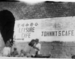 Signs in English for the "Leisure Cafe' (公余咖啡室) and "Johnny's Cafe painted on a town wall near a town gate in China during WWII.