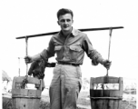 GI poses with buckets on a shoulder pole in China, during WWII.