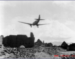 A US C-47 transport plane flies over a damaged village, probably outside of Kunming, Yunnan province.