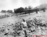 Kenneth Williams inspects a bomb crater at an American base in China during WWII. A C-46 transport is in the background.