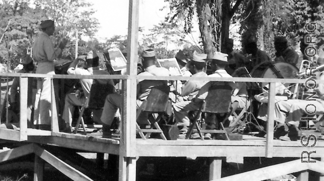 A convoy loaded with troops and engineers prepares to set out, while a band plays. Note that much of the band is African-American.  During WWII.