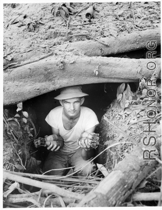 Engineer of the 797th Engineer Forestry Company poses in an old bunker with discarded Americans mortar shells in hand, similar to US M49A2 60MM mortar.  During WWII.