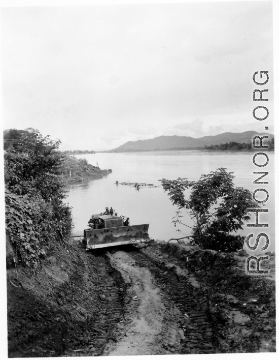 Caterpillar pulling logs raft up bank from river.  797th Engineer Forestry Company in Burma.  During WWII.