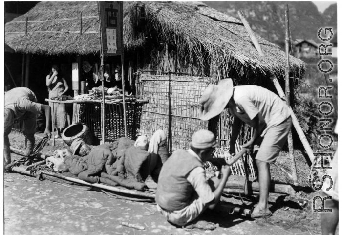 Stretcher bearers take a break in Guangxi province, either Guilin or Liuzhou area, probably during the evacuation of fall 1944. The white paper posted on the store sign says basically, "Everything for sale, including building, animals, possessions."