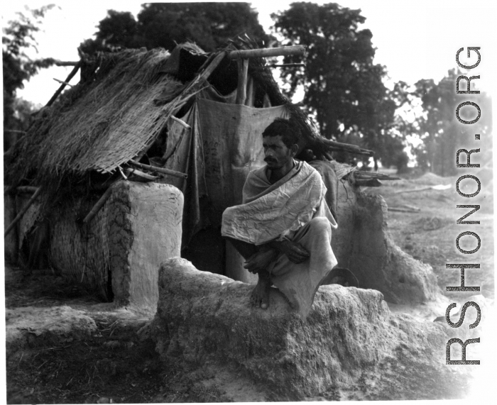 Man squatting on mud wall.  Scenes in India witnessed by American GIs during WWII. For many Americans of that era, with their limited experience traveling, the everyday sights and sounds overseas were new, intriguing, and photo worthy.