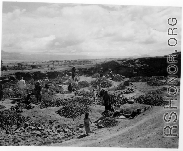 People crush rocks by hand.  Scenes in India witnessed by American GIs during WWII. For many Americans of that era, with their limited experience traveling, the everyday sights and sounds overseas were new, intriguing, and photo worthy.