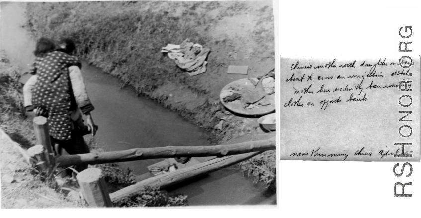 A mother carrying a baby crosses a ditch to get to the washing on the other side. April 1945. Near Kunming, China.