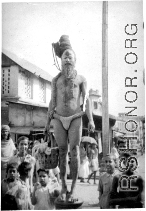 An Indian fakir and interested crowd look at cameraman during WWII.