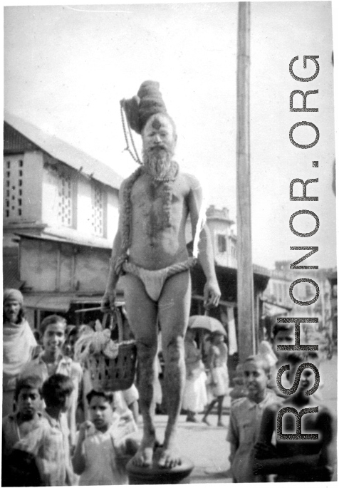 An Indian fakir and interested crowd look at cameraman during WWII.