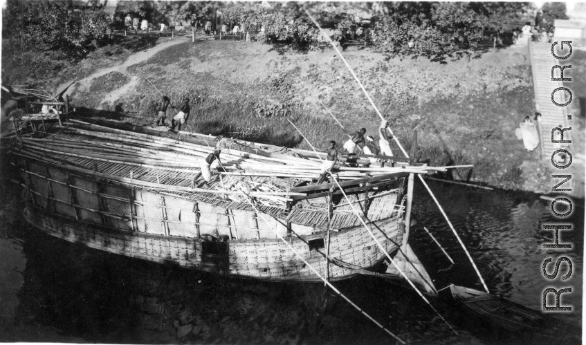Numerous boatmen use poles to push a large boat in a waterway in India during WWII.
