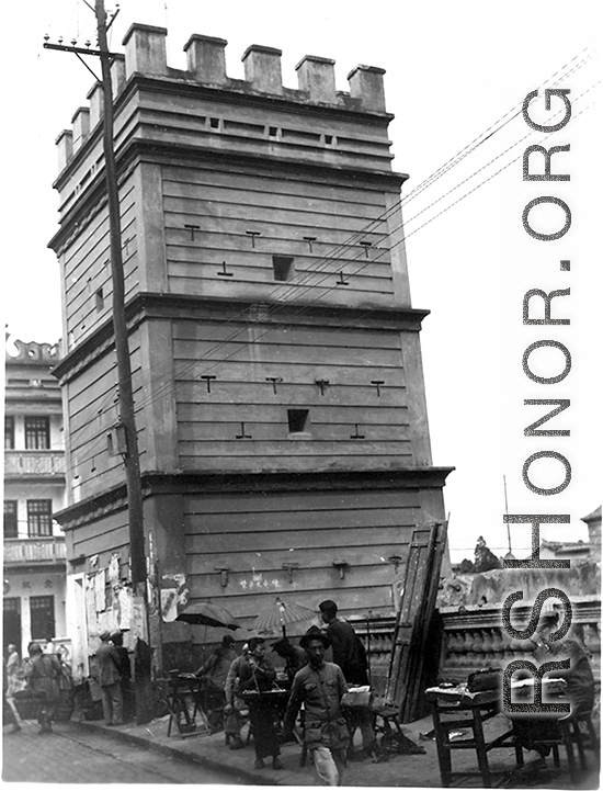 A gun tower fortress in Yunnan province, China, probably in Kunming city, during WWII. Note the desks set up for various kinds of business on the sidewalk in the foreground.