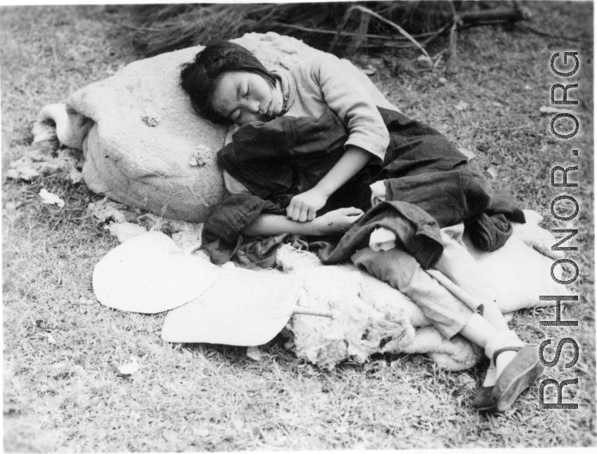 A woman sleeping, possibly cradling a baby: A tired, sick, or weakened refugee during the Chinese civilian evacuation in Liuzhou city, Guangxi province, China, during WWII, in the summer or fall of 1944 as the Japanese swept through as part of the large Ichigo push.