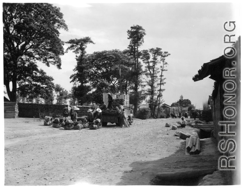 Local people in a village in Yunnan province, China loading or unloading a truck, with lumber and/or farm goods and livestock. During WWII.