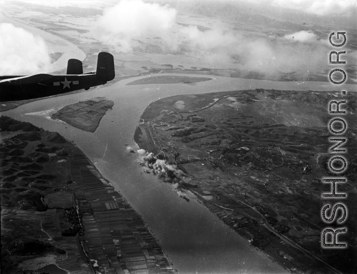 A Mitchell B-25, tail number 444, flies away from a site just bombed in China or Indochina area.