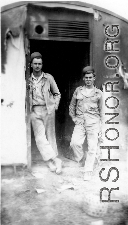 "Elmer Bukey and Chester Rush in the doorway of our engineering office at Liangshan,China. The holes and the damage seen are the results of nightly air raids by the Japanese. Our engineering area left a lot to be desired but it was amazing the amount of and the quality of the work that was performed by the men."