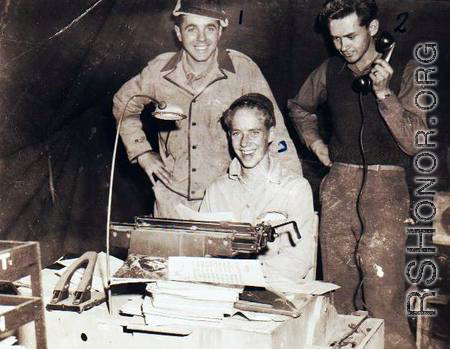 "Jim Kruger (standing), Elliot Knecht (seated), and an unknown member of the 396th having their picture taken in the Orderly Room."