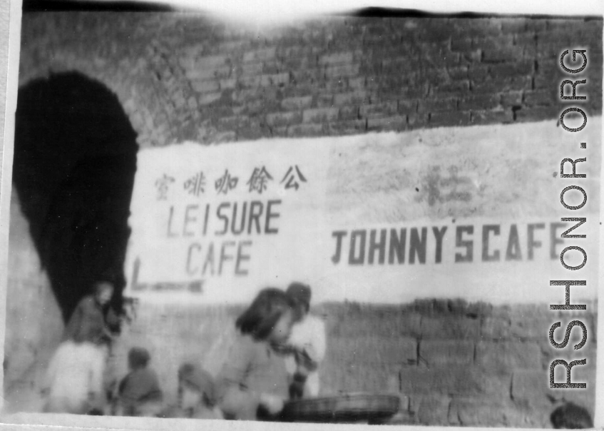 Signs in English for the "Leisure Cafe' (公余咖啡室) and "Johnny's Cafe painted on a town wall near a town gate in China during WWII.