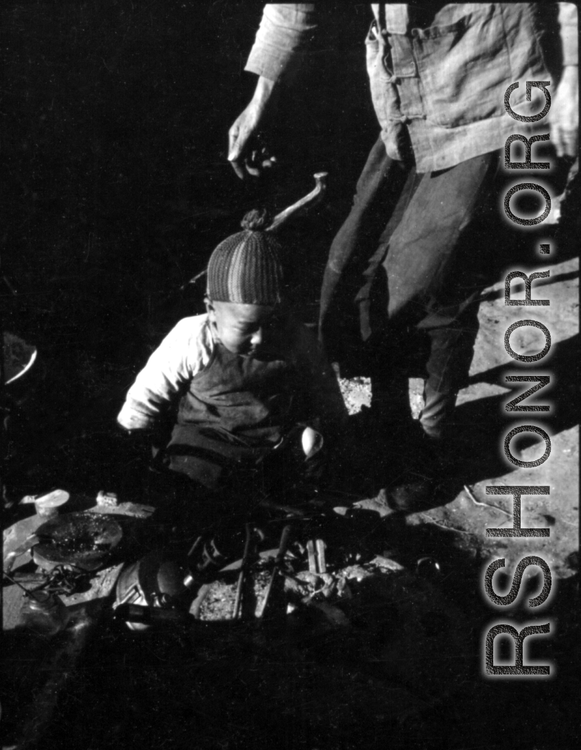 A small child plays at a charcoal hearth in China during WWII. These might be refugees at Liuzhou.